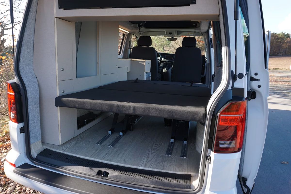 VW T6.1 in Kirschrot, Blick durch die offene Heckklappe auf Liegefläche und Küchenzeile