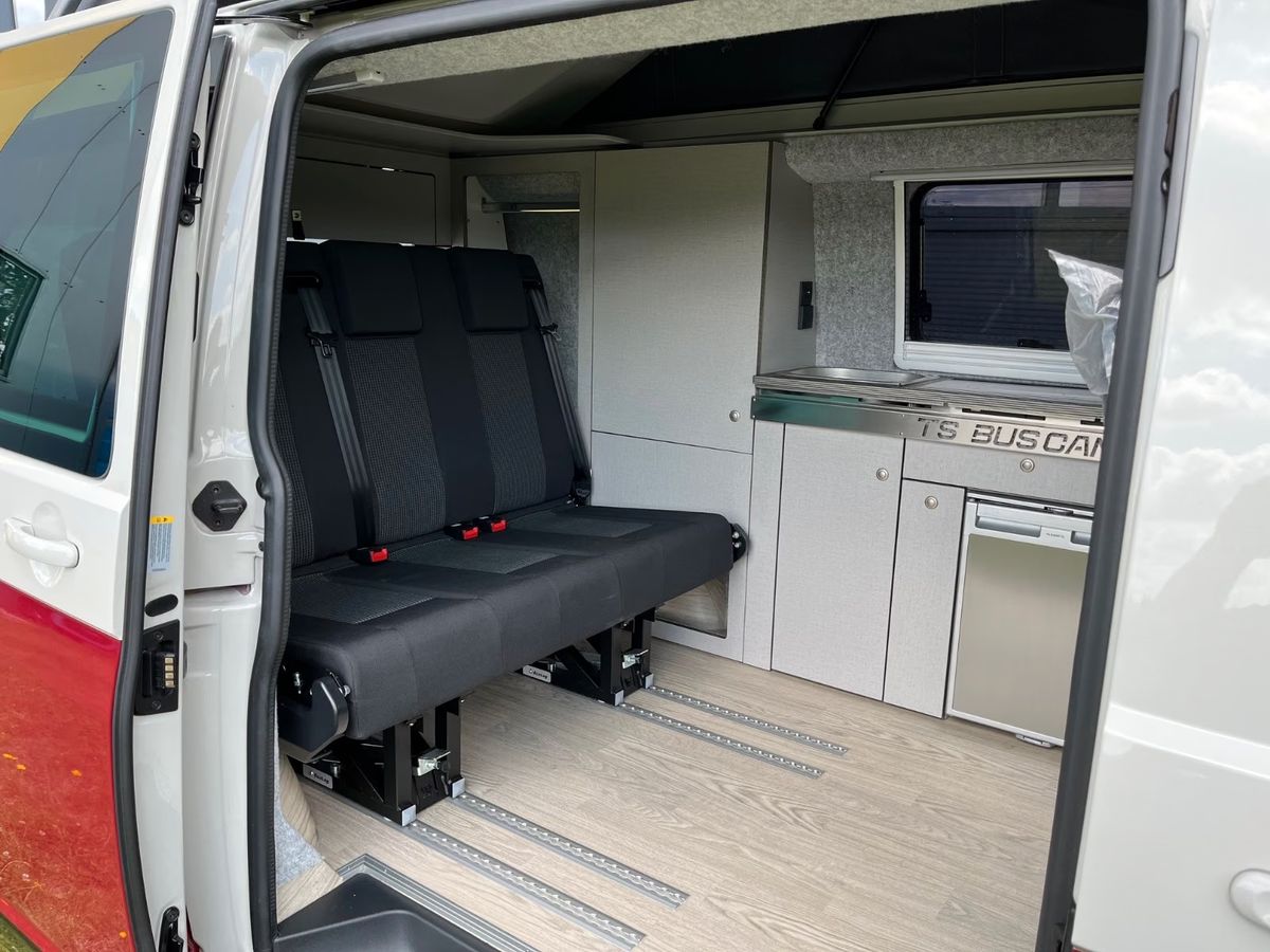VW T6.1 in Kirschrot, Blick durch die offene Schiebetür auf Sitzbank und Küchenzeile