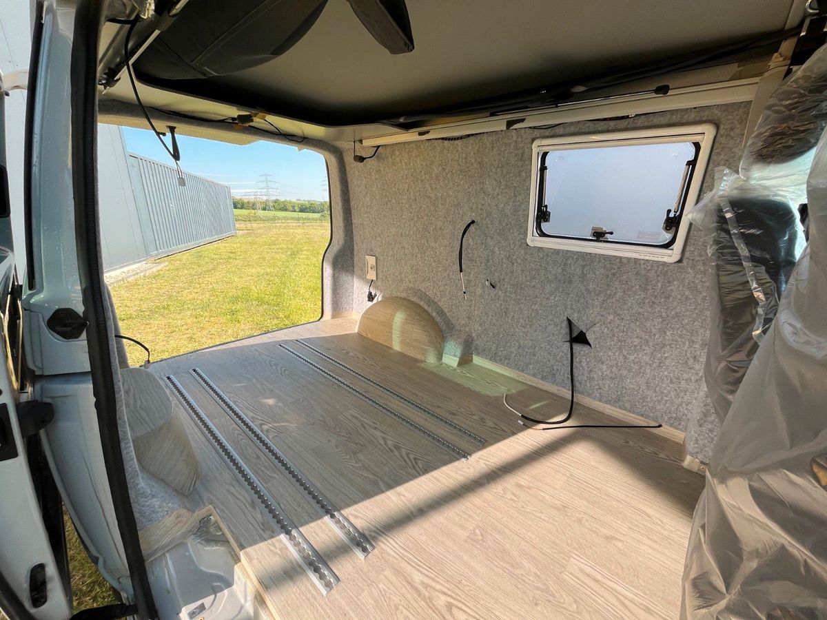 VW T6.1 in Hellrot/Ascotgrau, leerer Laderaum mit gefilzten Seitenwänden und Bodenschienen